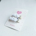 Détail de deux pinces à cheveux roses en satin blanc faites à la main sur carte de mode - Paire Blanche