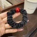 Nahaufnahme eines schwarzen Falten-Haargummis mit glänzend roter Perle am Handgelenk - Schwarzer Stoff mit Roter Perle (Gummiband)