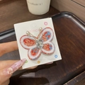 Détail d'une pince à cheveux papillon brodée rouge avec pompons et cristal brillant - Papillon Mixte Unique / 1 Pièce / Mélange Rouge et Bleu