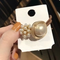 Detailaufnahme von braunem Haargummi mit großer Perle in Goldrahmen und Perlenverzierung - Beige
