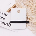 Detail shot of a black matte rectangular hair clip on a display card with a soft warm aesthetic - Black