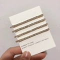Detailed view of four golden hair clips with sparkling white rhinestones on card - Gold Straight Row Fine Rhinestone Clips