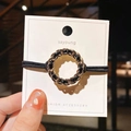 Close-up of golden chain and black leather woven hair tie on a white display card - Round Style