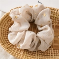 Detail eines cremefarbenen Chiffon-Scrunchie mit goldenen Sternen in einem Korb - Beige