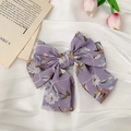 Detail view of lavender floral chiffon bow hair clip on elegant white satin background - Purple