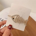 Détail macro d'une barrette poisson dorée avec strass blancs sur carte de présentation - Doré