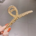 Elegante pinza de pelo de metal dorado con diseño de cadena sobre fondo gris minimalista - Oro Mate