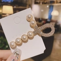 Detailed view of the elegant pearl hair clip with sparkling rhinestones on a gold base - Gold
