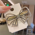 Dettaglio di un fermaglio per capelli a fiocco dorato con strass e accenti di linee nere - Stile Fiocco Grande Strass