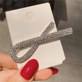 Détail d'une pince à cheveux argentée en X ornée de strass brillants sur son support - Croix Argent