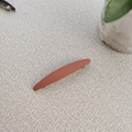 Close-up of matte terracotta rectangular hair clip with frosted texture on beige fabric - Orange