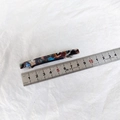Detalle de una pinza de acetato de 6,5 cm con patrón jaspeado colorido y regla de medir - Floral Negro