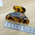 Detail view showing tortoise shell hair claw clip size measurement on wooden table - Vivid Colors