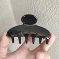 Nahaufnahme einer glänzend schwarzen Acetat-Haarklammer, von Hand gehalten vor Texturwand - Schwarz