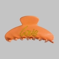 Detail van een glanzende oranje haarklem met gele strassteentjes in de vorm van Love - Oranjegeel