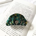 Dettaglio di un fermaglio per capelli marmorizzato vintage su un libro con texture verde - Fiori Verdi