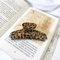 Detail einer großen Haarklammer mit Schildpatt-Mosaik-Textur auf einem Buch - Braun Floral