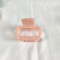 Detailed macro view of small pink marble acetate hair claw clip on white fabric - Pink Series