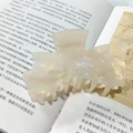 Pearlescent ivory acetate hair claw clip with bow design resting on a book - Mermaid White