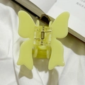 Close-up of a light yellow butterfly-shaped acetate hair claw clip on a white fabric background - Yellow-Green