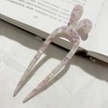 Dettaglio di una forcina per capelli in acetato marmorizzato viola su un libro - Floreale Viola Bianco