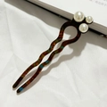 Detail van een U-vormige haarspeld met amberkleurig schelppatroon en drie witte parels - Amberbruin