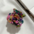 Draufsicht auf eine bunte Rosen-Haarklammer auf weißem Stoff mit Buchdetails - Rosa Blumenmuster