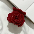 Detailansicht einer glänzenden dunkelroten Rosen-Haarklammer auf einem Buch - Dunkelrot