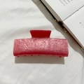 Gros plan sur une pince à cheveux en acrylique rose marbré sur fond de tissu blanc doux - Rouge pastèque