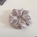 Detail eines Lavendel-Scrunchies mit Blumenmuster, Waffelstruktur und Markenlabel - Reisgrau