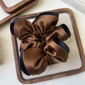 Close-up of brown satin scrunchie with black velvet edges on a wooden tray - Brown