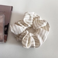 Détail d'un chouchou en tissu rayé crème avec texture plissée douce et éclairage tamisé - Abricot Riz