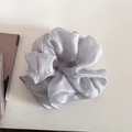 Detail of silver-grey satin scrunchie with glossy silk texture and elegant folds on a table - Gray