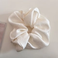 Nahaufnahme von cremefarbenem Satin-Haargummi mit glitzernden Pailletten und Faltenstruktur - Cremeweiß