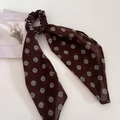 Primo piano di elastico marrone a pois con nastri su uno sfondo bianco pulito - Scrunchie con Nastro / Marrone