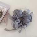 Détail d'un chouchou en tulle gris avec longs rubans sur une surface crème épurée - Bleu gris