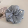Détail macro d'un chouchou en organza bleu clair avec broderie florale de marguerites - Bleu