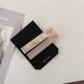 Detailed macro view of two marble acetate hair clips with gold lettering on black card - Creamy White