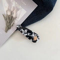 Makroaufnahme einer marmorierten Acetat-Haarklammer mit goldenem Logo auf Denim - Schwarz-Weiß-Muster