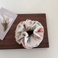 Vue détaillée d'un chouchou floral avec des motifs rouges et verts sur tissu beige - Style Bouton de Fleur / Style 1 Choucou Bourgeon de Fleur