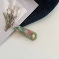 Nahaufnahme der Haarspange aus Acetat mit Marmormuster und goldenem Logo-Detail - Rosa & Grün