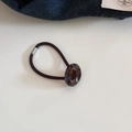 Dettaglio ravvicinato del bottone in resina tartarugata su un elastico nero per capelli - Marmo Blu Caffè
