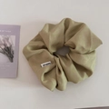 Vista detallada de un scrunchie de satén verde oliva hecho a mano con una etiqueta tejida - Verde