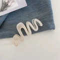 Detail der cremeweißen Haarklammer mit Wellenform und Perlmuttglanz auf Denim - Verlauf Aprikose