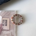 Detail eines orange-grünen Karo-Haargummis, das auf einer transparenten CD-Hülle liegt - Braun