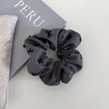 Detailweergave van grijze scrunchie met strikpatroon op een witte tafel met props - Basis Grijs