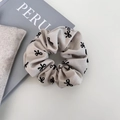 Detail van een beige scrunchie met zwarte strikpatronen op textuurstof en een boek - Basis Wit