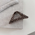 Detailopname van geometrische haarklem met luipaardprint op een boekachtergrond - Driehoek Stijl