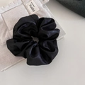 Detail van een zwarte satijnen scrunchie met zijdeglans textuur op een beige stof - Zwart