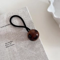 Dettaglio dell'elastico per capelli con sfera tartarugata lucida su un libro - 1# Sfera Caffè Scuro